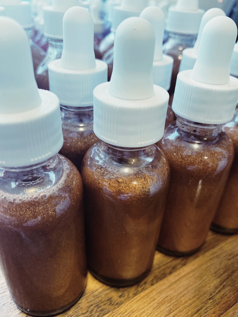 May include: A group of small glass bottles with white dropper tops filled with a shimmering brown liquid. The bottles are arranged in a row on a wooden surface.