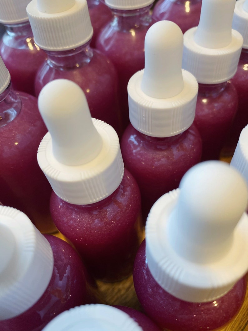 K&ouml;nnte beinhalten: Eine Gruppe kleiner Glasflaschen mit wei&szlig;en Tropfern, gef&uuml;llt mit einer schimmernden rosa Fl&uuml;ssigkeit. Die Flaschen sind in einer Nahaufnahme angeordnet.
