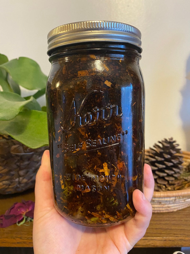 May include: A clear glass jar with a silver lid filled with a dark brown liquid and various herbs and plant materials. The jar is labeled "Kerr" and "Self Sealing".