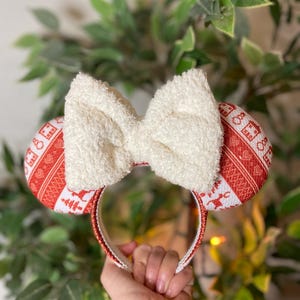 May include: Red and white patterned Minnie Mouse ears with a white fuzzy bow. The ears have a white headband.