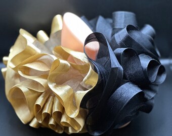 May include: A large, fluffy hair bow made of black and gold ribbon. The bow is tied in a large, loose knot and has a lot of volume.