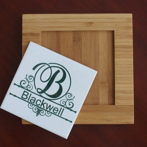 May include: A white ceramic tile with a dark green monogram "B" and the name "Blackwell" in a decorative font. The tile is placed on a bamboo coaster with a square recessed area.