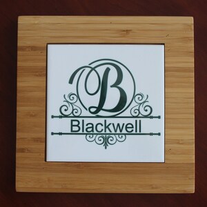 May include: Square bamboo coaster with a white tile insert. The tile features a dark green monogram "B" with decorative flourishes and the name "Blackwell" below. The coaster has a natural wood grain finish.