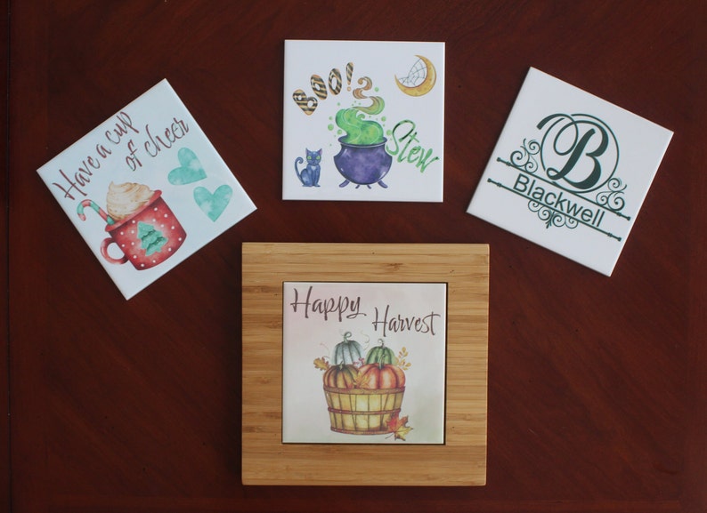 May include: Four decorative ceramic tiles with various designs. One tile features a mug with the text "Have a cup of cheer". Another says "Boo! 2 Stew" with a cauldron. A third tile has the name "Blackwell". The last tile says "Happy Harvest" with pumpkins.