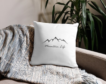 May include: White throw pillow with a black mountain range silhouette and the text "Mountain Life" printed on it.