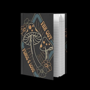 May include: A black notebook with a mushroom design and the words "Far Out Peace & Love". The notebook features a diamond-shaped design with two mushrooms and floral accents in shades of orange and teal. The notebook is open, revealing lined pages.