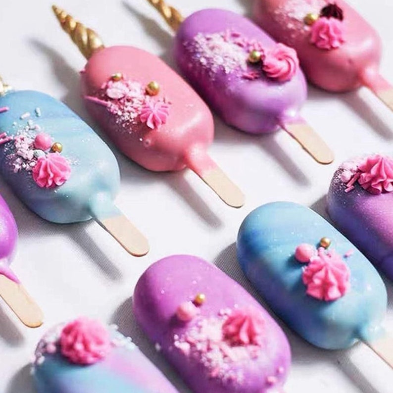 May include: A collection of unicorn-themed cake pops with a variety of colors, including pink, purple, blue, and white. The cake pops are decorated with sprinkles, edible glitter, and gold horns.