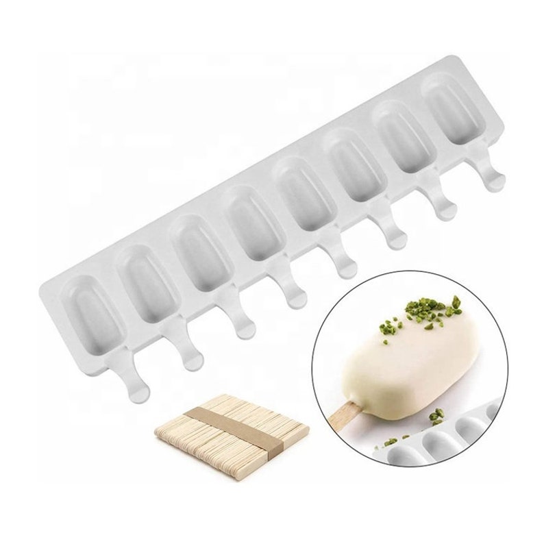 May include: White silicone popsicle mold with eight individual molds and attached sticks. The mold is on a white surface. A wooden popsicle stick is shown next to the mold.