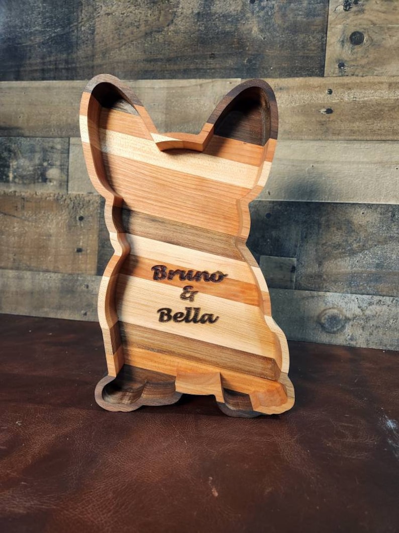Pu&ograve; includere: Un vassoio di servizio in legno a forma di cane con una finitura in legno naturale. Il vassoio &egrave; inciso con i nomi "Bruno & Bella".