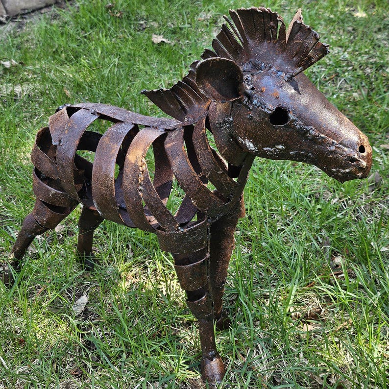 Puede incluir: Escultura de metal oxidado que representa una cebra. El cuerpo est&aacute; hecho de tiras de metal soldadas, creando un efecto de jaula. La escultura est&aacute; sobre hierba verde. La cabeza y la melena est&aacute;n detalladas. Una pieza decorativa para el jard&iacute;n.