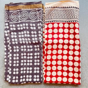 Peut inclure: Deux torchons en tissu, l'un avec un fond gris et des pois blancs, l'autre avec un fond rouge et des pois blancs. Les deux torchons ont une bordure décorative.