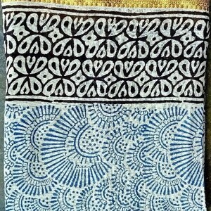 May include: A white cotton fabric with a blue and white floral pattern. The fabric has a gold trim along the top edge.