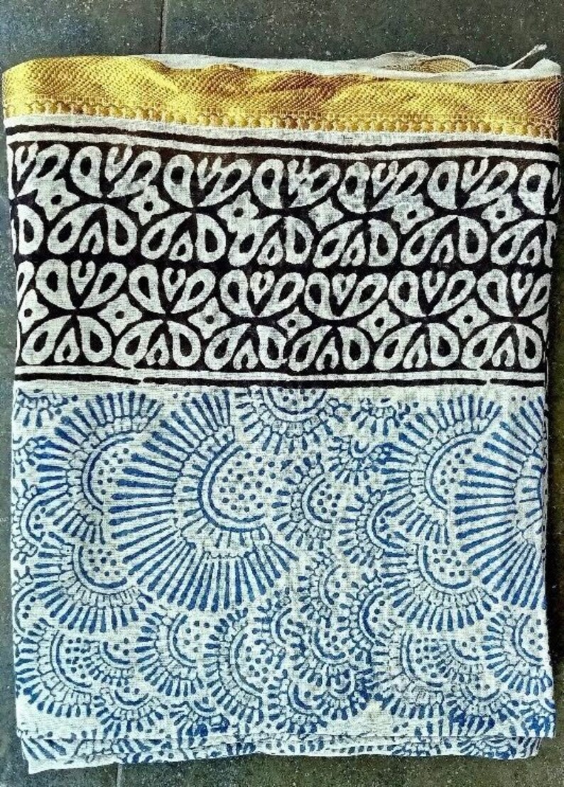 May include: A white cotton fabric with a blue and white floral pattern. The fabric has a gold trim along the top edge.