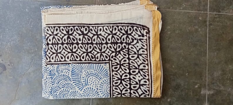 May include: A white cotton fabric with a black and blue block print design. The fabric has a gold border.