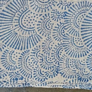 May include: A white fabric tablecloth with a blue and white floral pattern. The pattern is made up of small circles and lines.