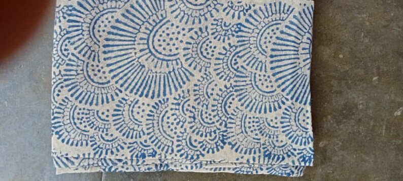 May include: A white fabric tablecloth with a blue and white floral pattern. The pattern is made up of small circles and lines.