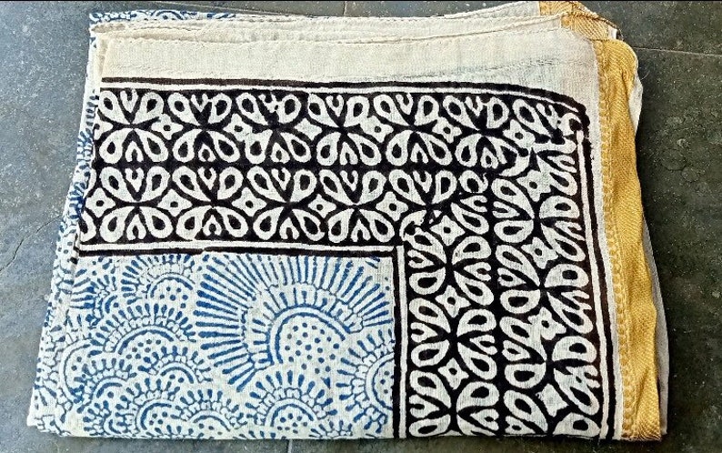May include: A white cotton scarf with a black and blue geometric pattern. The scarf has a gold border.