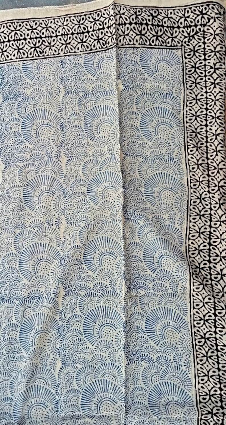 May include: A white cotton fabric with a blue and black printed design. The fabric features a repeating pattern of stylized floral motifs.