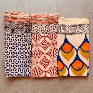 May include: Three cotton scarves with different block printed patterns. The first scarf has a blue and white geometric pattern, the second scarf has a red and white floral pattern, and the third scarf has a blue, orange and yellow peacock feather pattern.