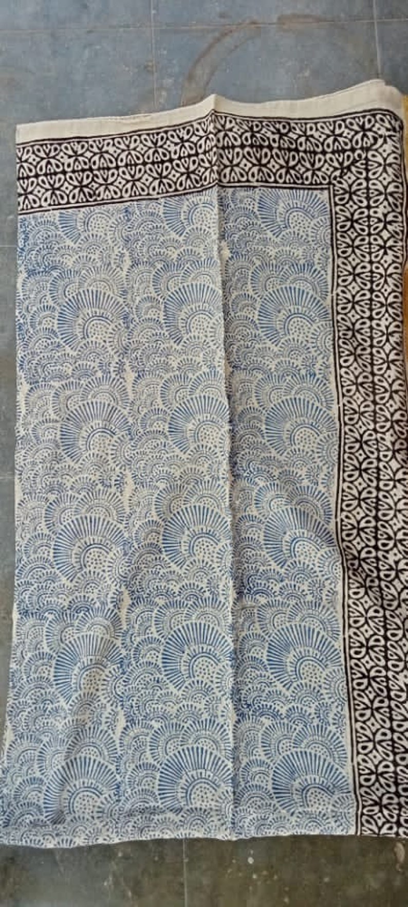 May include: A white fabric with a blue and black block print design. The fabric has a repeating pattern of stylized fans.