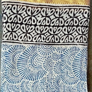 May include: A white cotton fabric with a blue and white floral pattern. The fabric has a gold trim and a black and white border with a geometric pattern.