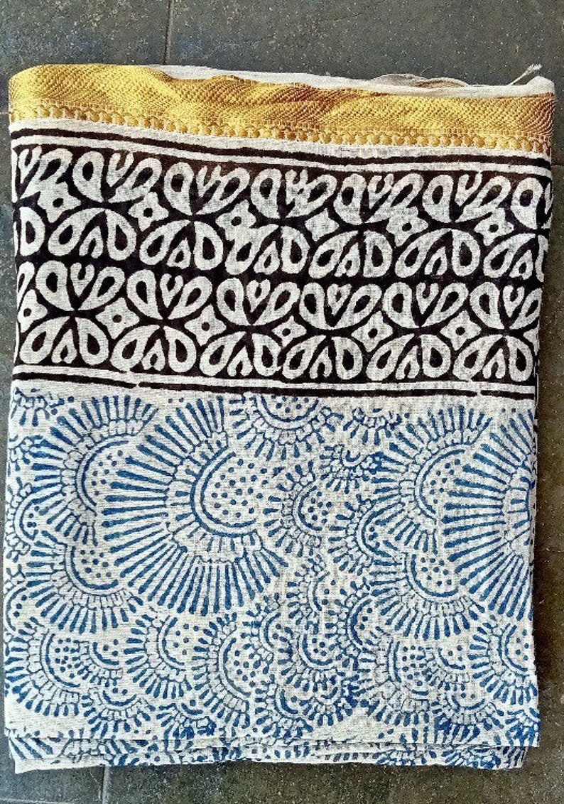 May include: A white cotton fabric with a blue and white floral pattern. The fabric has a gold trim and a black and white border with a geometric pattern.