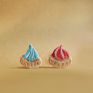 Pode incluir: Dois patches bordados em forma de pastel com um redemoinho de glacê no topo. Um patch tem glacê azul e o outro tem glacê rosa.