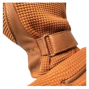 May include: A brown leather strap with a gold buckle is attached to a brown knitted fabric. The fabric has a textured pattern.