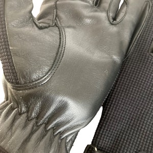 May include: A pair of black leather gloves with a textured wrist cuff. The gloves have a seam down the back of the hand and a small white mark on the palm.