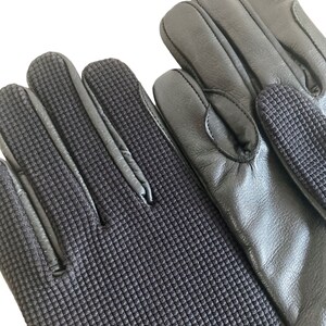 May include: A pair of black leather gloves with a textured fabric on the fingertips and palm. The gloves have a smooth leather back.