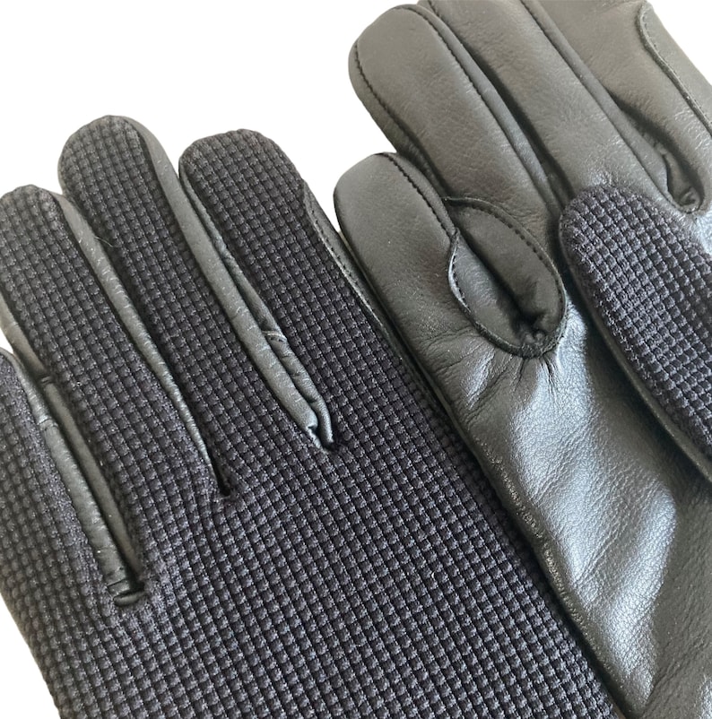 May include: A pair of black leather gloves with a textured fabric on the fingertips and palm. The gloves have a smooth leather back.