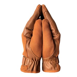 May include: A pair of brown leather gloves with a textured fabric on the back of the hand. The gloves are folded together with the fingertips touching.