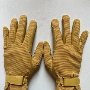 May include: A pair of yellow leather gloves with a textured pattern. The gloves have a strap with a buckle on the wrist.