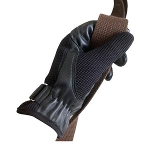May include: A black leather and mesh riding glove with a brown strap. The glove has a buckle closure and a textured palm.