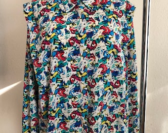 May include: A white long-sleeved button-up shirt with a colorful abstract print. The print features shades of blue, green, yellow, red, and black.