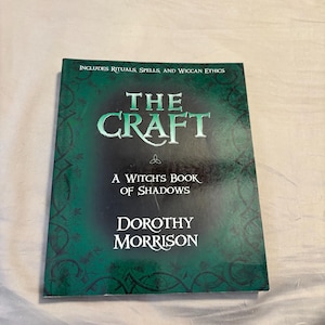May include: A green book with the title "The Craft: A Witch's Book of Shadows" by Dorothy Morrison. The book cover features an ornate design and the text "Includes Rituals, Spells, and Wiccan Ethics".
