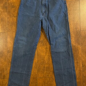 Puede incluir: Un par de pantalones vaqueros de mezclilla azul oscuro con corte recto. Los pantalones tienen un dise&ntilde;o cl&aacute;sico de cinco bolsillos y cierre de bot&oacute;n.