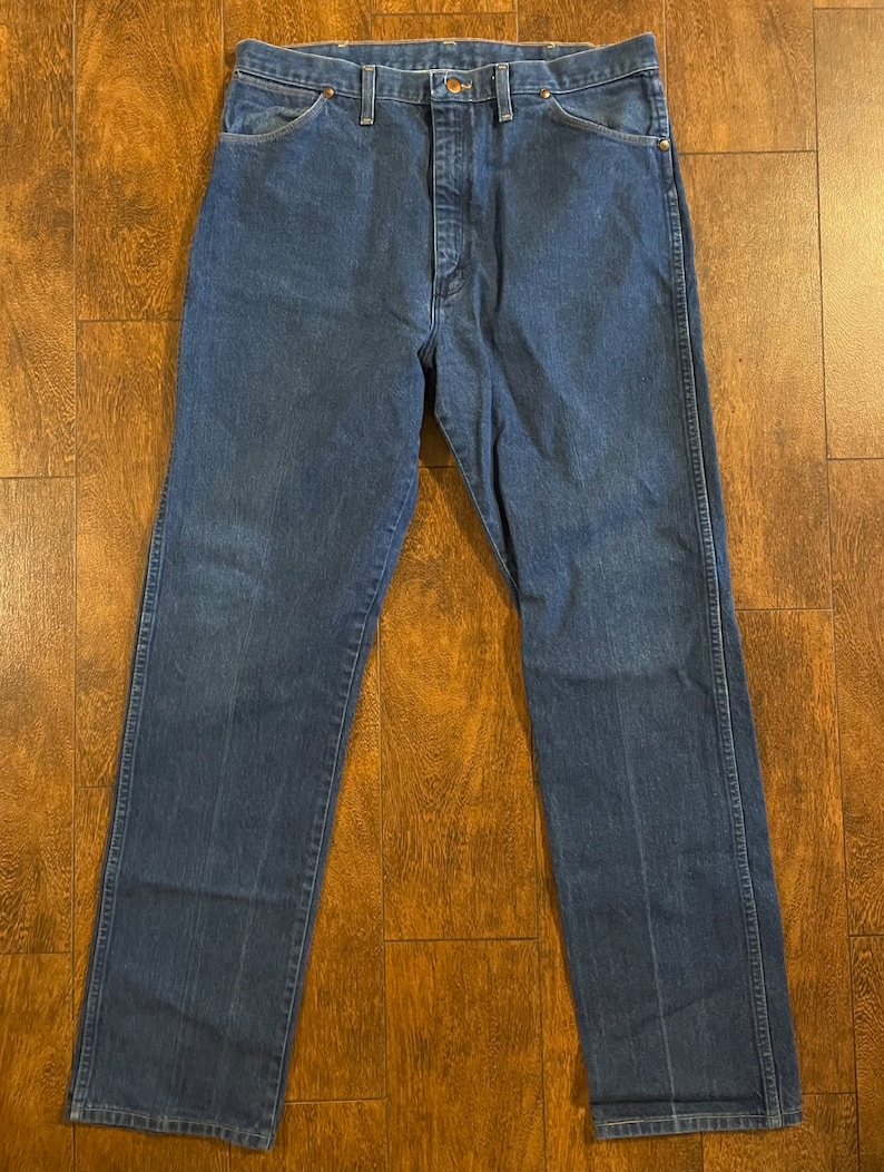 Puede incluir: Un par de pantalones vaqueros de mezclilla azul oscuro con corte recto. Los pantalones tienen un dise&ntilde;o cl&aacute;sico de cinco bolsillos y cierre de bot&oacute;n.