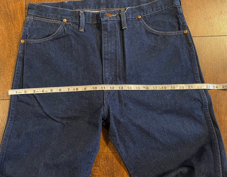 Puede incluir: Un par de pantalones vaqueros de mezclilla azul oscuro con corte recto. Los vaqueros tienen un dise&ntilde;o cl&aacute;sico de cinco bolsillos y cierre de bot&oacute;n. La medida de la cintura es de 63,5 cm.