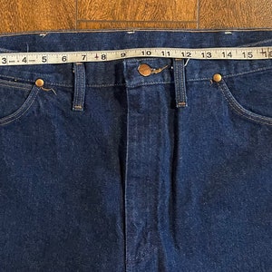 Puede incluir: Un par de pantalones vaqueros de mezclilla azul oscuro con un ojal para cintur&oacute;n de cuero marr&oacute;n y un cierre de bot&oacute;n met&aacute;lico. Los pantalones vaqueros se miden con una cinta m&eacute;trica, mostrando una talla de cintura de 46 cm.