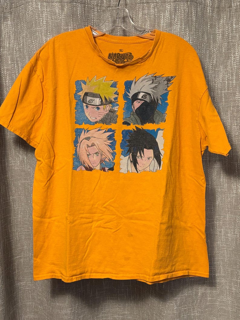 Puede incluir: Una camiseta de manga corta de color naranja brillante con un estampado gr&aacute;fico de cuatro personajes de Naruto en cuadrados individuales con borde azul. La etiqueta interior del cuello muestra el logo de Naruto y la talla XL. Cuello redondo.