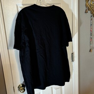 May include: A black t-shirt hanging on a hanger. The t-shirt is plain with no visible graphics or text.