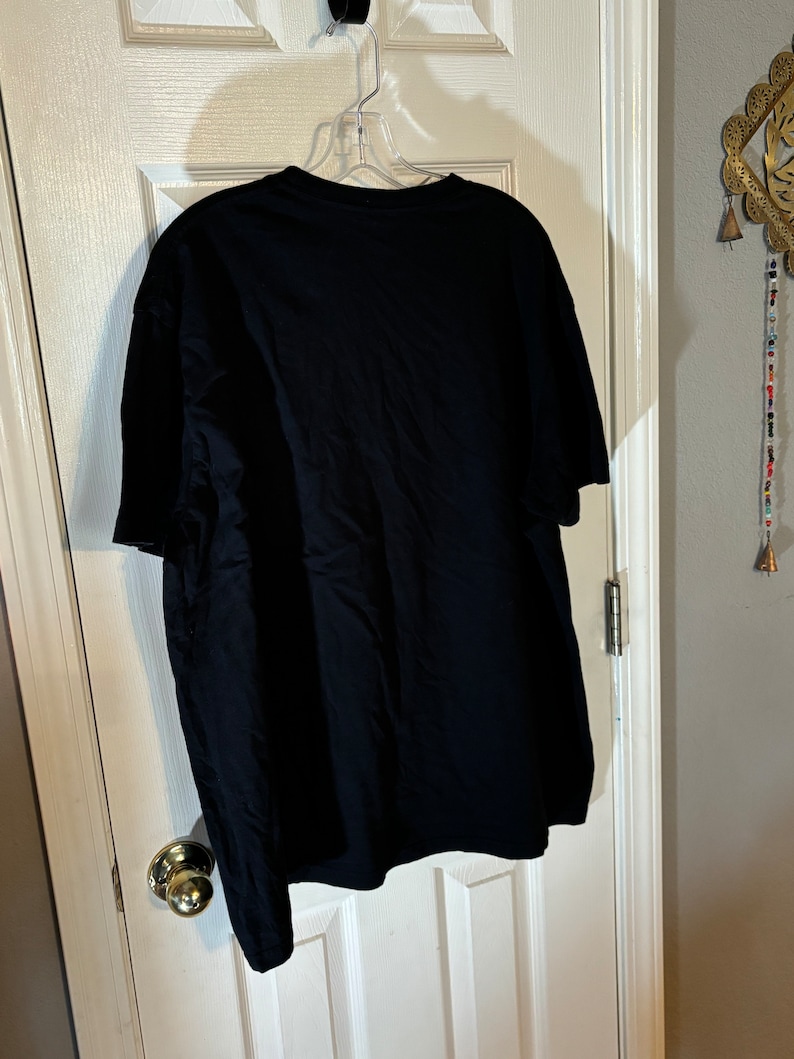May include: A black t-shirt hanging on a hanger. The t-shirt is plain with no visible graphics or text.