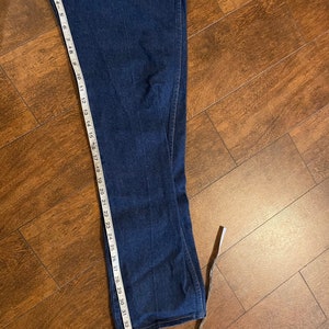 Puede incluir: Un par de pantalones vaqueros de mezclilla azul oscuro con una cinta m&eacute;trica blanca que se extiende desde el dobladillo inferior. La cinta mide 94 cm.