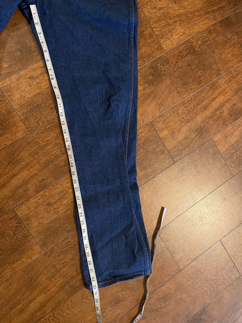 Puede incluir: Un par de pantalones vaqueros de mezclilla azul oscuro con una cinta m&eacute;trica blanca que se extiende desde el dobladillo inferior. La cinta mide 94 cm.