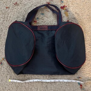 May include: Navy blue tote bag with two rounded side pockets and a rectangular center. The bag has burgundy trim and handles, with a burgundy and navy blue strap. A measuring tape shows the bag is approximately 16 inches wide.