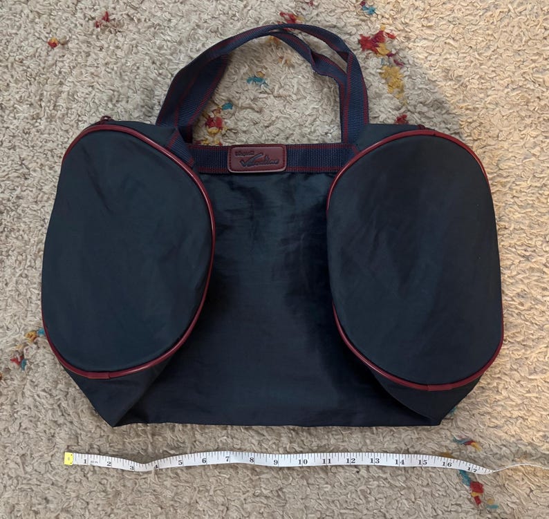 May include: Navy blue tote bag with two rounded side pockets and a rectangular center. The bag has burgundy trim and handles, with a burgundy and navy blue strap. A measuring tape shows the bag is approximately 16 inches wide.