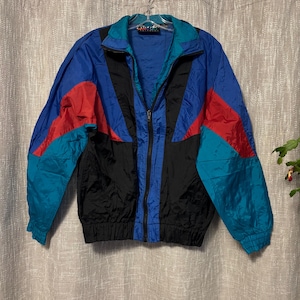 May include: A vintage color block jacket in blue, black, red, and teal. The jacket has a full zipper, a stand-up collar, and elastic cuffs and hem. The jacket is hanging on a hanger.