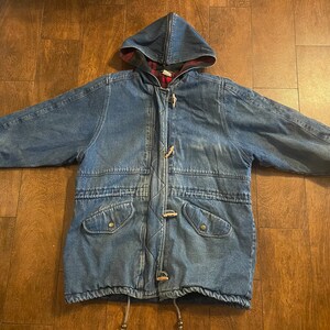 May include: A blue denim jacket with a plaid lining in the hood. The jacket has a zipper closure, toggle closures, and two flap pockets.