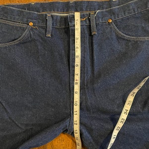 Puede incluir: Un par de pantalones vaqueros de mezclilla azul oscuro con una cinta m&eacute;trica que corre verticalmente por la costura central. La cinta mide 40,6 cm.